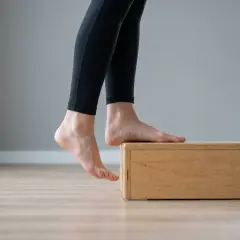 Esercizi per fascite plantare: piedi nudi su un rialzo di legno, tallone abbassato per allungare.
