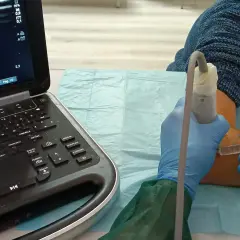 Ecografia guidata per infiltrazioni al gomito. Un medico con guanti blu esegue un'iniezione sotto guida ecografica.