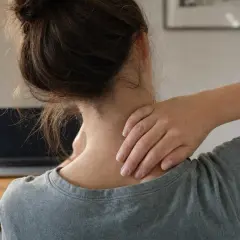 Donna con il collo che scricchiola, massaggiandosi la nuca mentre lavora al computer.