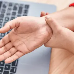 Mano che si tiene il polso, forse per dolori o fitte al polso, vicino a un laptop.