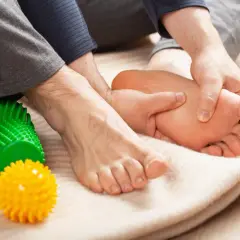Mani che massaggiano il piede, alleviando il dolore del neuroma di Morton. Palline massaggianti colorate a lato.