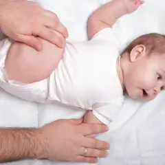 Mani adulte che controllano le anche di un neonato, un esame per la displasia dell'anca.