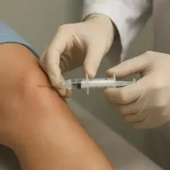Mani guantate eseguono infiltrazioni al ginocchio con una siringa, un trattamento per alleviare il dolore.