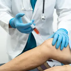 Medico in guanti blu inietta PRP nel ginocchio di un paziente. La terapia PRP può accelerare i tempi di recupero.