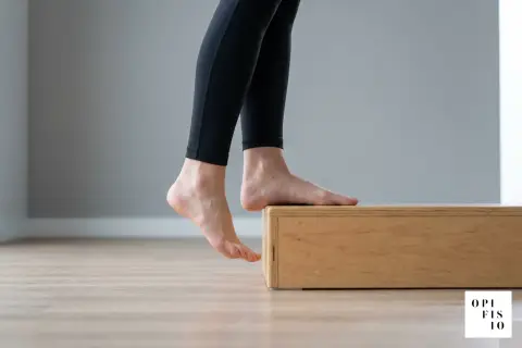 Esercizi per fascite plantare: piedi nudi su un rialzo di legno, tallone abbassato per allungare.