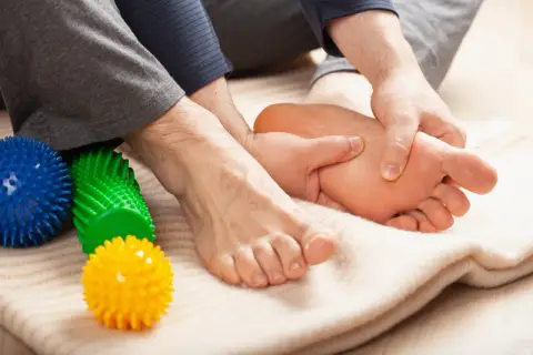 Mani che massaggiano il piede, alleviando il dolore del neuroma di Morton. Palline massaggianti colorate a lato.