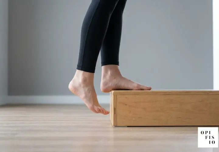 Esercizi per fascite plantare: piedi nudi su un rialzo di legno, tallone abbassato per allungare.