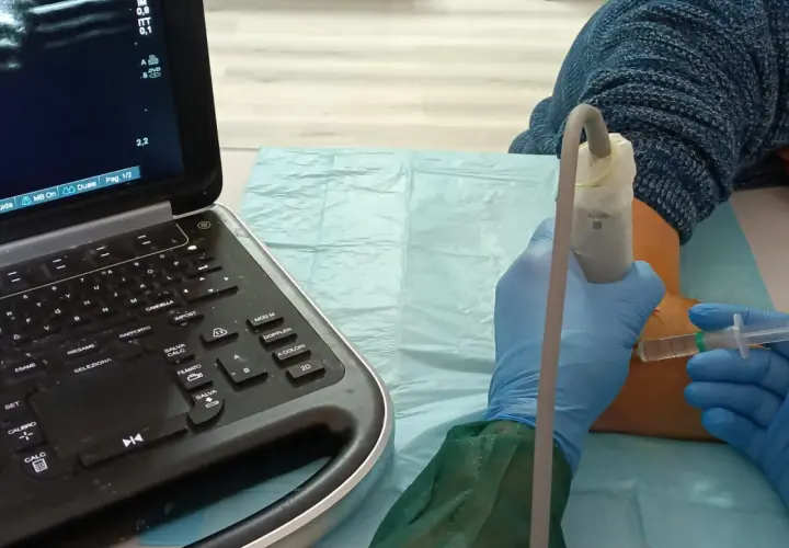 Ecografia guidata per infiltrazioni al gomito. Un medico con guanti blu esegue un'iniezione sotto guida ecografica.