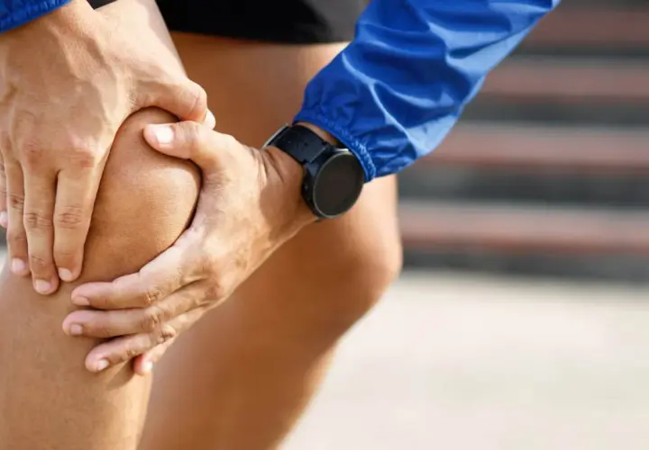 Atleta con le mani sul ginocchio, soffre di infiammazione tendine rotuleo. Indossa un orologio sportivo.