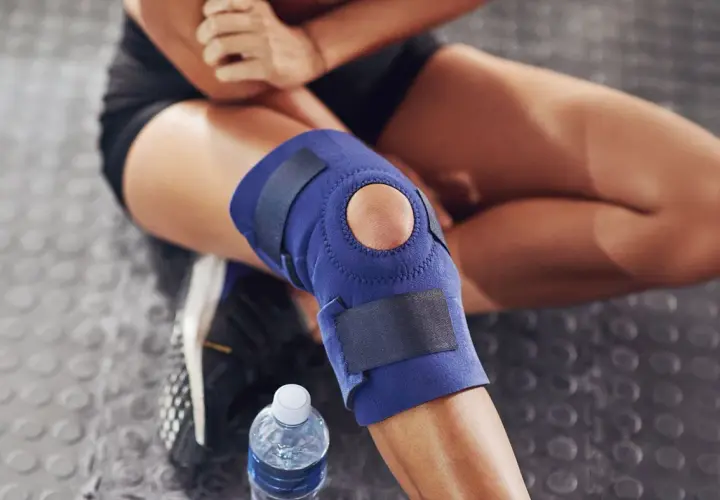 Donna con tutore al ginocchio blu, seduta su pavimento gommato. Considerare le controindicazioni del tutore ginocchio prima dell'uso.