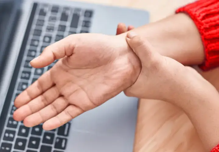 Mano che si tiene il polso, forse per dolori o fitte al polso, vicino a un laptop.