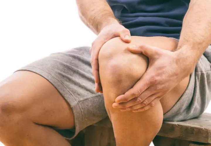 Uomo con mani sul ginocchio, segno di sovraccarico ginocchio e lunghi tempi di recupero.