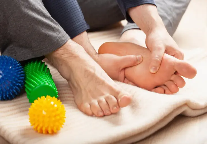 Mani che massaggiano il piede, alleviando il dolore del neuroma di Morton. Palline massaggianti colorate a lato.