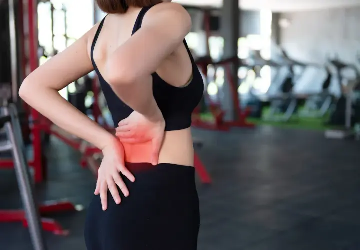Donna in palestra con dolore ai muscoli lombari, evidenziato in rosso.