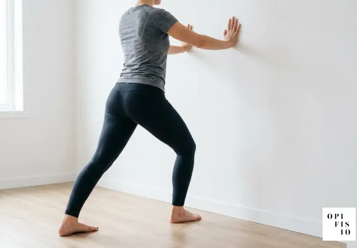 Donna esegue stretching per tallonite appoggiandosi al muro. Esercizi per il benessere del piede.