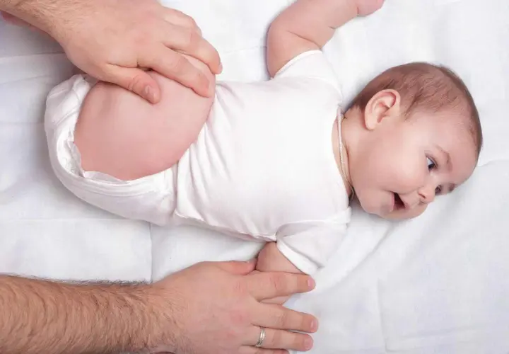 Mani adulte che controllano le anche di un neonato, un esame per la displasia dell'anca.