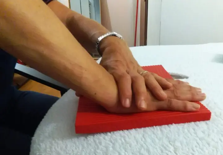 Mani che si appoggiano su un tappetino rosso, un gesto che può far parte dei rizoartrosi rimedi per alleviare il dolore.