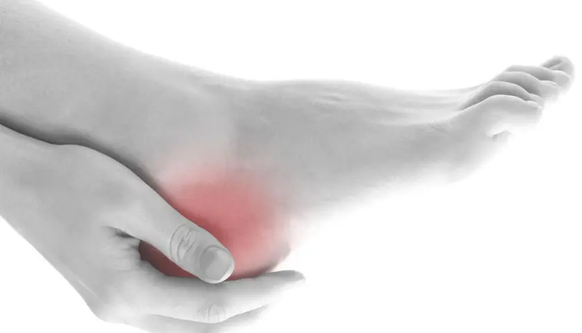 Mano che massaggia un tallone arrossato, indicando dolore ai talloni a letto.