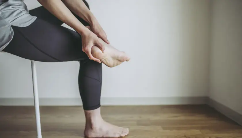 Persona che si massaggia il tallone, forse per un dolore o per le cause di un male al tallone.