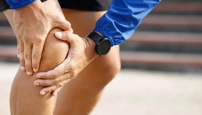 Atleta con le mani sul ginocchio, soffre di infiammazione tendine rotuleo. Indossa un orologio sportivo.
