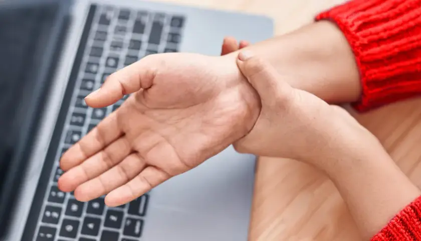Mano che si tiene il polso, forse per dolori o fitte al polso, vicino a un laptop.