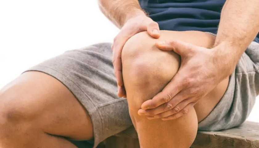 Uomo con mani sul ginocchio, segno di sovraccarico ginocchio e lunghi tempi di recupero.