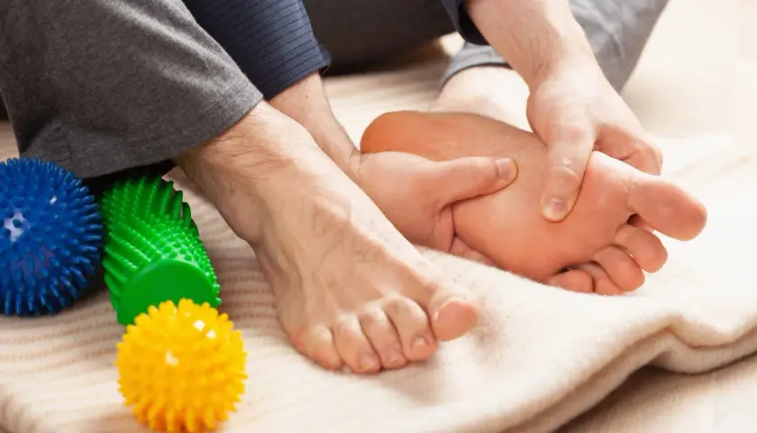 Mani che massaggiano il piede, alleviando il dolore del neuroma di Morton. Palline massaggianti colorate a lato.