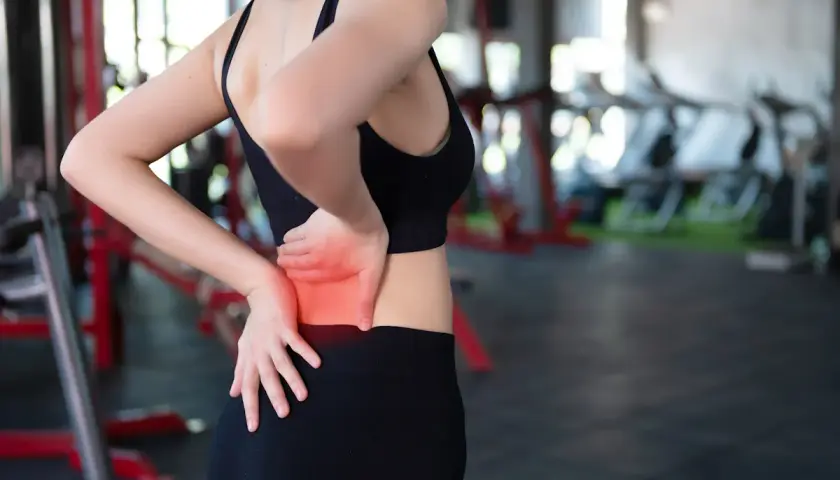 Donna in palestra con dolore ai muscoli lombari, evidenziato in rosso.