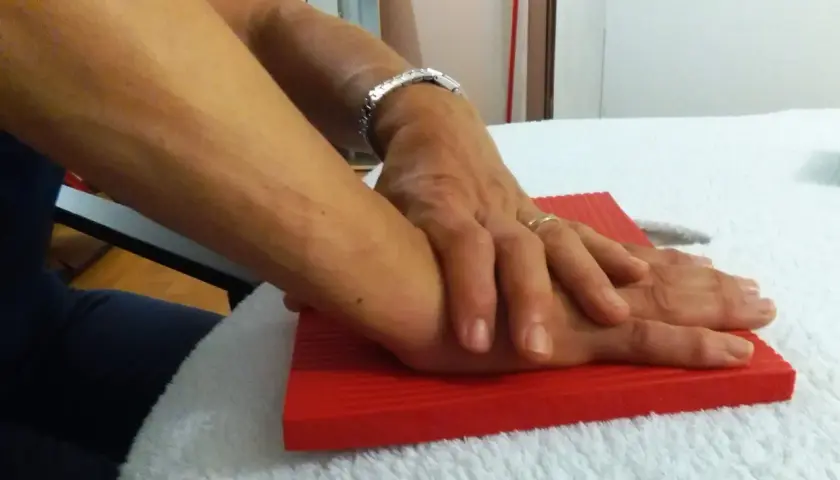 Mani che si appoggiano su un tappetino rosso, un gesto che può far parte dei rizoartrosi rimedi per alleviare il dolore.