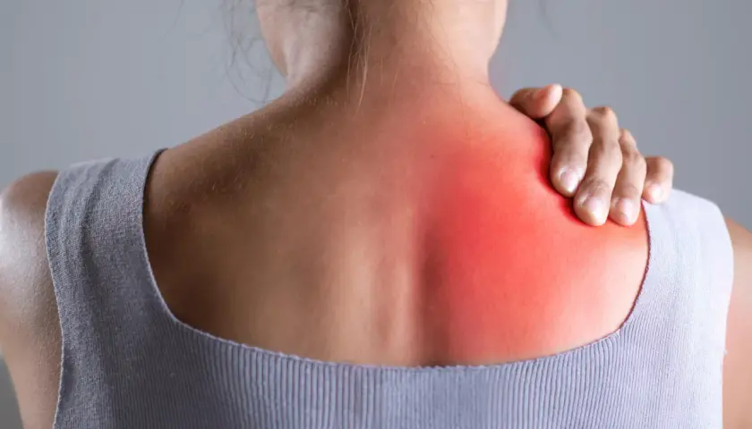 Donna con mano sulla spalla sinistra, evidenziata in rosso, per indicare bruciore sotto la scapola sinistra: cause e rimedi.