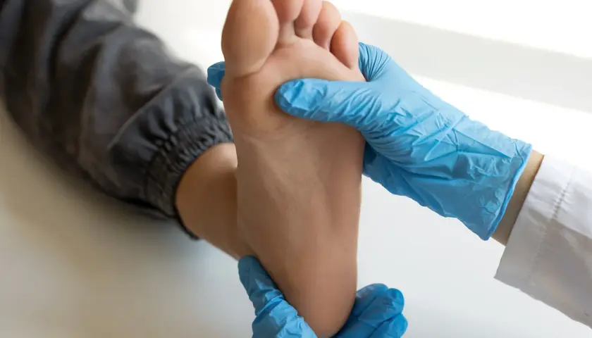Mani guantate esaminano un piede, cercando sollievo per il dolore sotto le dita del piede con rimedi naturali.