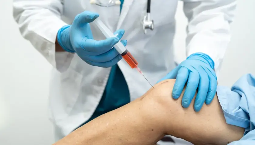 Medico in guanti blu inietta PRP nel ginocchio di un paziente. La terapia PRP può accelerare i tempi di recupero.
