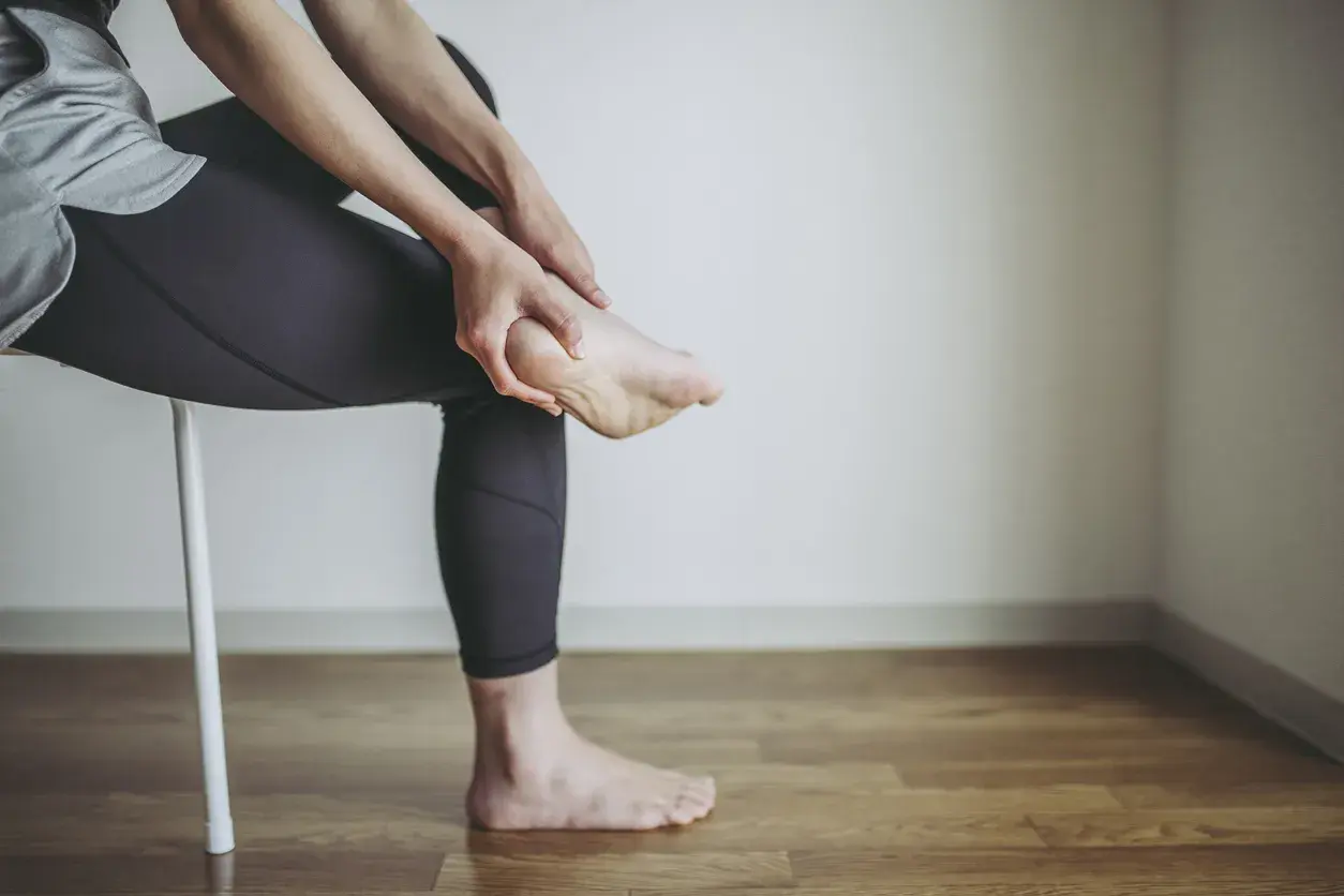 Persona che si massaggia il tallone, forse per un dolore o per le cause di un male al tallone.