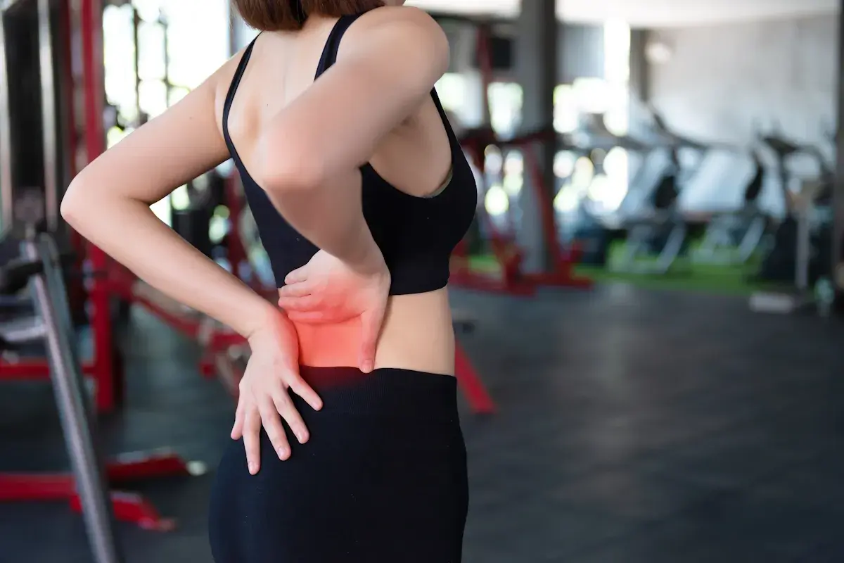 Donna in palestra con dolore ai muscoli lombari, evidenziato in rosso.