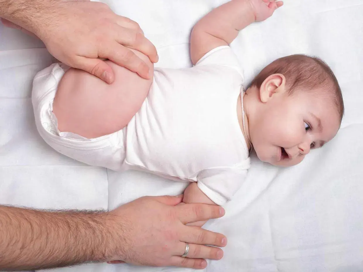 Mani adulte che controllano le anche di un neonato, un esame per la displasia dell'anca.