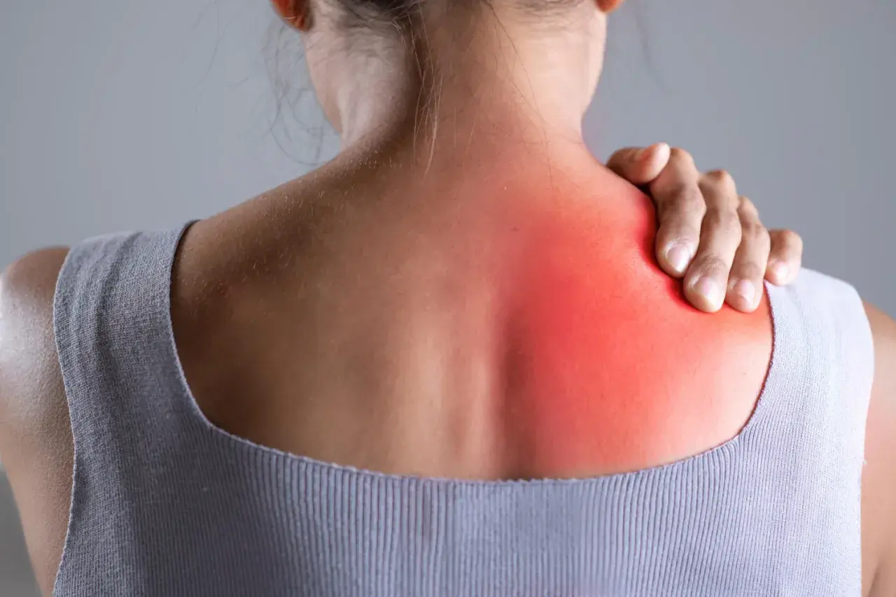 Donna con mano sulla spalla sinistra, evidenziata in rosso, per indicare bruciore sotto la scapola sinistra: cause e rimedi.