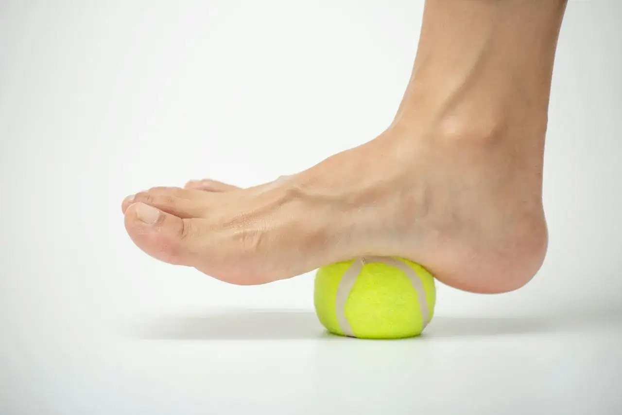 Piede che rotola su una pallina da tennis per alleviare la fascite plantare. Utile anche il magnesio per i crampi.