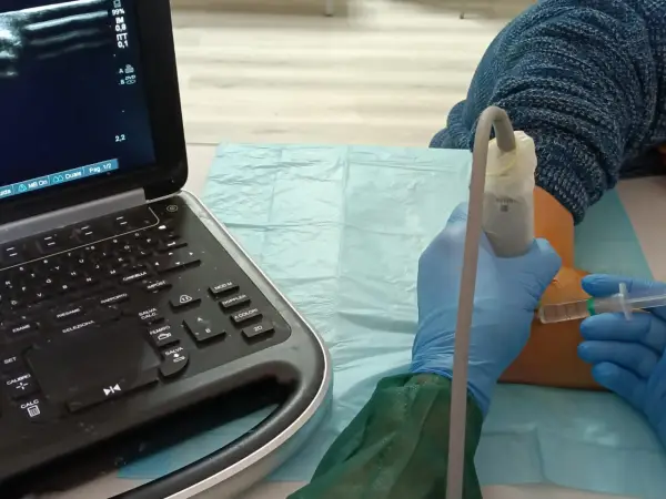 Ecografia guidata per infiltrazioni al gomito. Un medico con guanti blu esegue un'iniezione sotto guida ecografica.