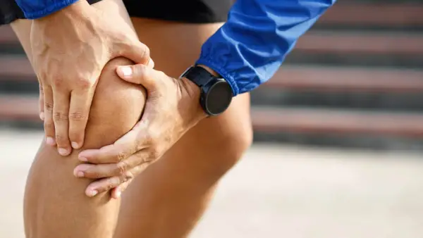 Atleta con le mani sul ginocchio, soffre di infiammazione tendine rotuleo. Indossa un orologio sportivo.